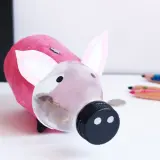 Urocza skarbonka diy z butelki, ozdobiona różowym papierem i uszami. W jej brzuszku widać monety.