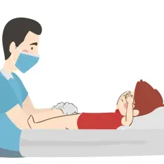 Ilustracja pokazuje, kiedy odciągać napletek u chłopca. Lekarz w masce i rękawiczkach delikatnie bada dziecko leżące na łóżku.