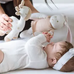 3 miesięczne dziecko nie chwyta zabawek, ale z zaciekawieniem patrzy na pluszową żyrafkę i królika podawane przez mamę.