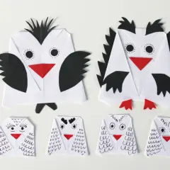 Dwie duże i cztery małe sowy z papieru, wykonane techniką origami. Każda sowa z papieru ma czerwony dziób i czarne detale.