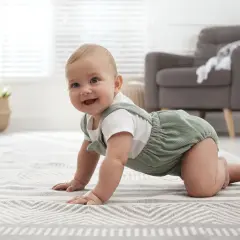 Uśmiechnięte, 8-miesięczne dziecko nie siedzi, ale z radością raczkuje po dywanie w salonie.