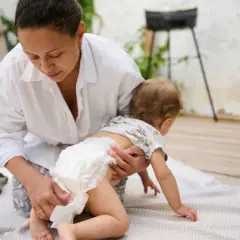 Mama zmienia pieluszkę, a maluch próbuje raczkować. Czasem zdarza się rzadka kupka u niemowlaka, ale mama sobie poradzi.