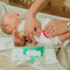 Delikatne dłonie mamy pokazują, jak przewijać noworodka, używając chusteczek nawilżanych.