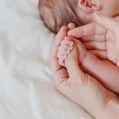 Delikatna dłoń rodzica obejmuje maleńką rączkę niemowlęcia. Octenisept na trądzik niemowlęcy to rozwiązanie dla wrażliwej skóry.