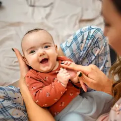 Uśmiechnięte 2 miesięczne dziecko co potrafi: łapać za palce, gaworzyć i cieszyć się bliskością mamy.
