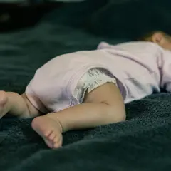 Małe nóżki i pupa noworodka w pieluszce, śpiącego na brzuchu. Czy noworodek może spać na brzuchu? Bezpieczeństwo przede wszystkim.
