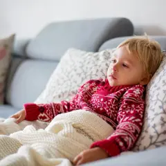 Chłopiec z gorączką, przykryty kocem, leży na kanapie. Obok pudełko chusteczek. Może to być początek drgawek gorączkowych.