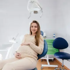Uśmiechnięta, ciężarna dentystka w gabinecie, czeka na pacjenta.