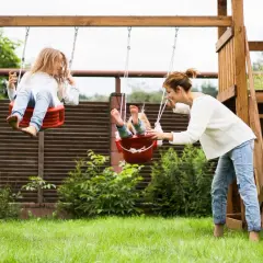Mama pcha huśtawki, zapewniając dzieciom radosne zabawy ruchowe na świeżym powietrzu.