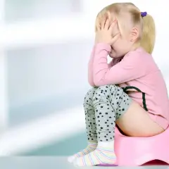 Smutna dziewczynka na nocniku, zakrywająca twarz dłońmi. Może to być objaw zapalenia dróg moczowych u dziecka.