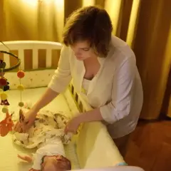 Mama uspokaja dziecko w łóżeczku, by złagodzić lęk separacyjny u niemowląt. Nad łóżeczkiem wisi karuzela z leśnymi zwierzątkami.