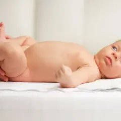 Nowe życie, delikatne nóżki i mały, czerwony pępek. Dziecko leży na białym tle, otoczone troską.