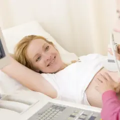 Uśmiechnięta przyszła mama podczas badania USG. Na ekranie widać obraz płodu, który odpowiada wielkości dziecka w 10 tygodniu ciąży.