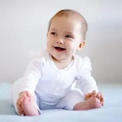 Uśmiechnięte dziecko siedzi na kolanach, zastanawiając się, czy 5 miesięczne dziecko można sadzać na kolanach.