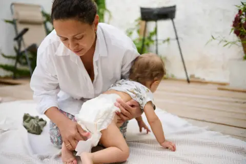 Mama zmienia pieluszkę, a maluch próbuje raczkować. Czasem zdarza się rzadka kupka u niemowlaka, ale mama sobie poradzi.