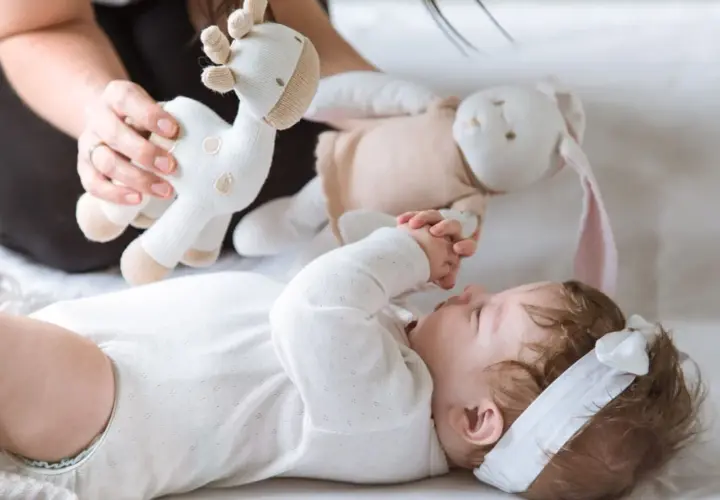 3 miesięczne dziecko nie chwyta zabawek, ale z zaciekawieniem patrzy na pluszową żyrafkę i królika podawane przez mamę.