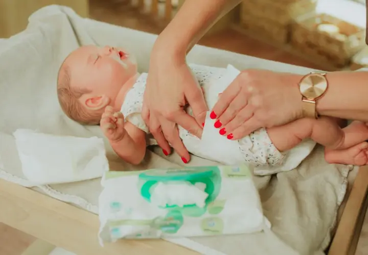 Delikatne dłonie mamy pokazują, jak przewijać noworodka, używając chusteczek nawilżanych.