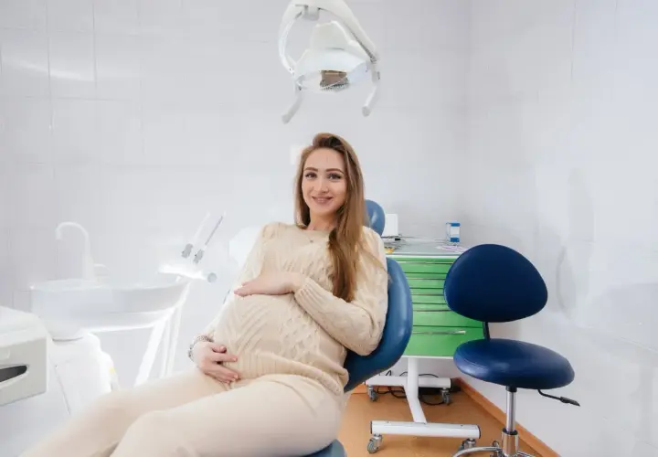 Uśmiechnięta, ciężarna dentystka w gabinecie, czeka na pacjenta.