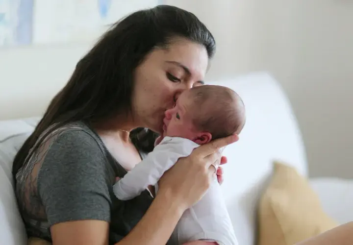 Ciepły uścisk mamy dla jej 6 tygodniowego dziecka. Delikatny pocałunek na czole maluszka.