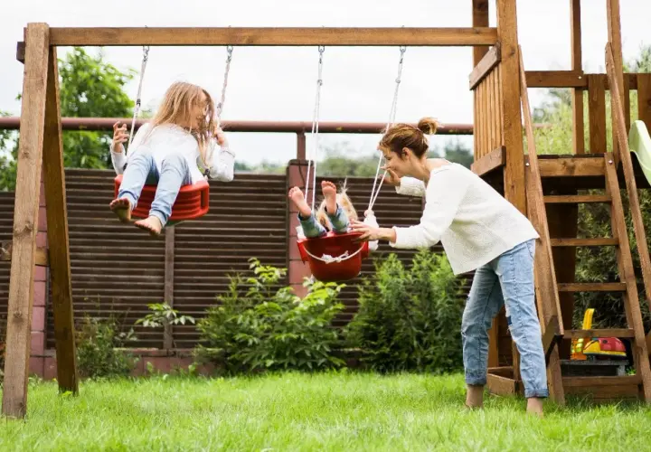 Mama pcha huśtawki, zapewniając dzieciom radosne zabawy ruchowe na świeżym powietrzu.