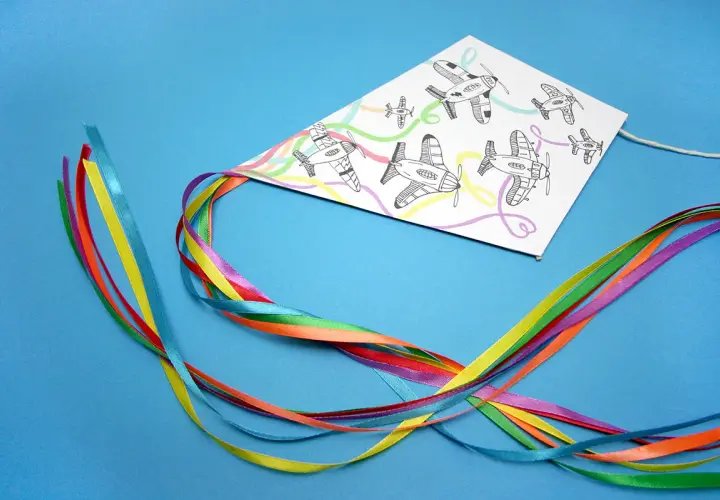 Kolorowy latawiec DIY z samolotami na tle niebieskim. Wstążki w tęczowych barwach tworzą ogon.