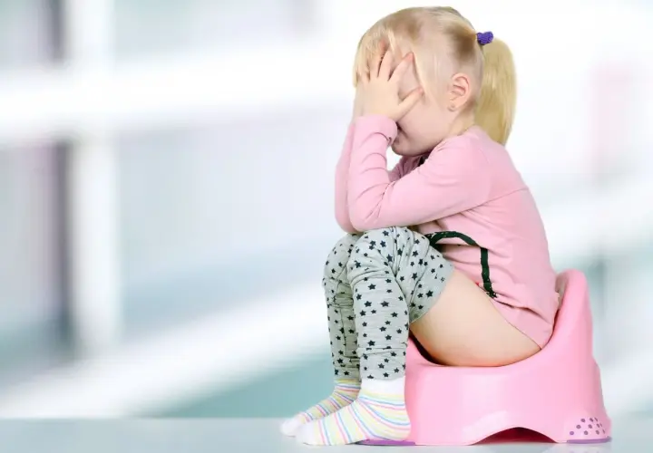 Smutna dziewczynka na nocniku, zakrywająca twarz dłońmi. Może to być objaw zapalenia dróg moczowych u dziecka.
