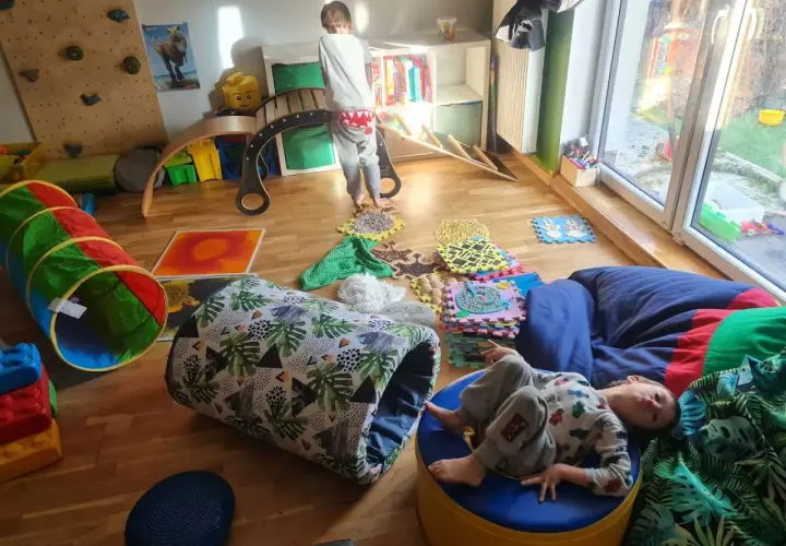 Dzieci bawią się na domowym torze przeszkód: tunel, ścieżka sensoryczna, ścianka wspinaczkowa i bujak.