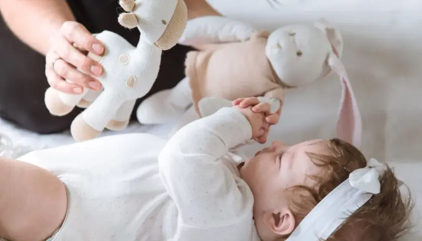 3 miesięczne dziecko nie chwyta zabawek, ale z zaciekawieniem patrzy na pluszową żyrafkę i królika podawane przez mamę.