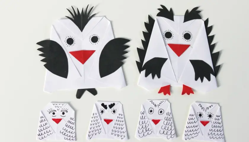 Dwie duże i cztery małe sowy z papieru, wykonane techniką origami. Każda sowa z papieru ma czerwony dziób i czarne detale.