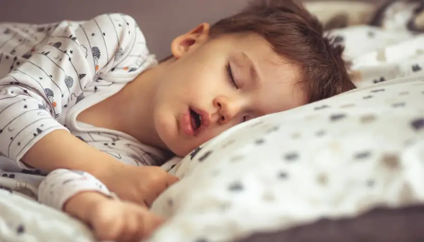 Małe dziecko śpi z otwartą buzią, wtulone w poduszkę. Jego sen jest głęboki i spokojny.