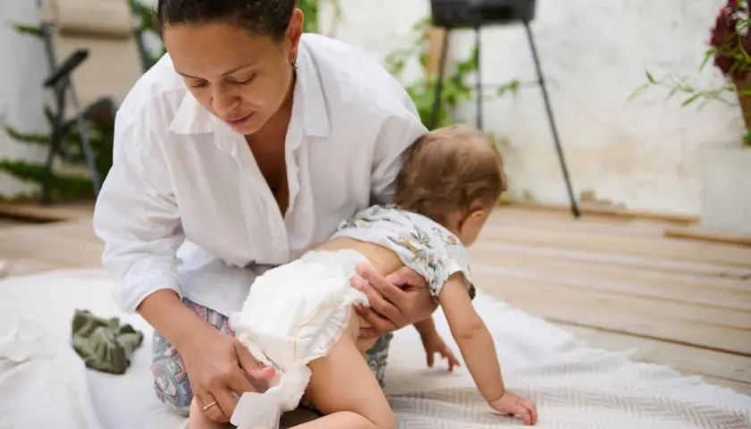 Mama zmienia pieluszkę, a maluch próbuje raczkować. Czasem zdarza się rzadka kupka u niemowlaka, ale mama sobie poradzi.