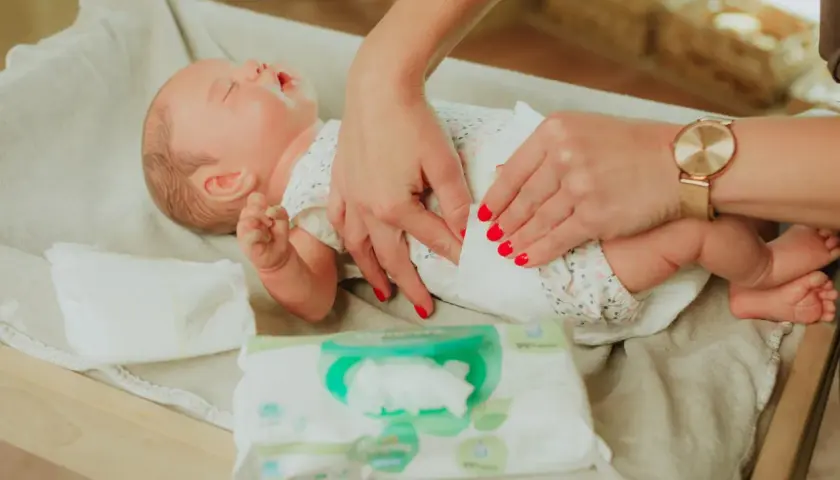 Delikatne dłonie mamy pokazują, jak przewijać noworodka, używając chusteczek nawilżanych.