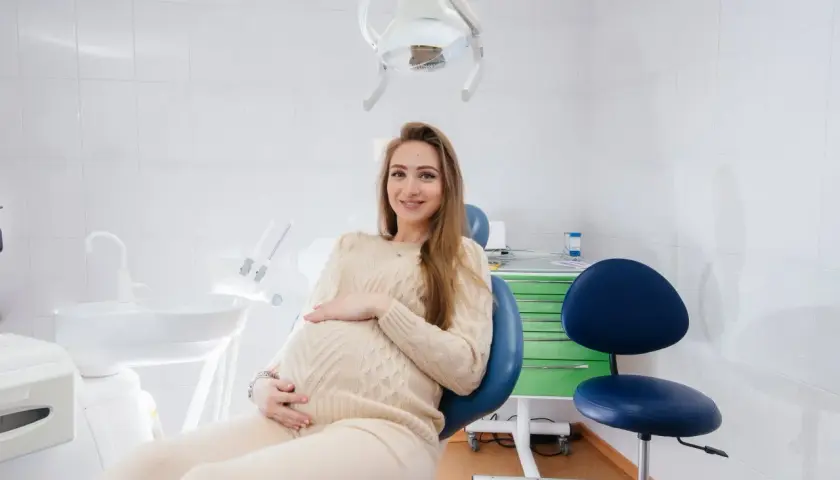 Uśmiechnięta, ciężarna dentystka w gabinecie, czeka na pacjenta.