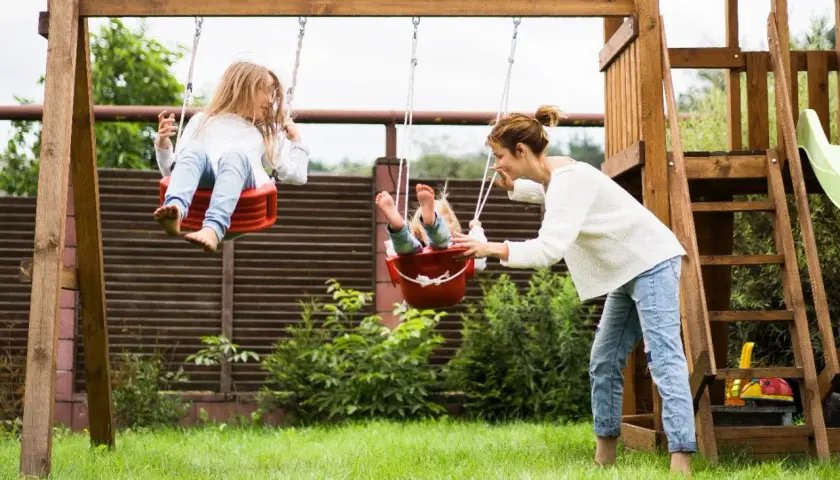Mama pcha huśtawki, zapewniając dzieciom radosne zabawy ruchowe na świeżym powietrzu.
