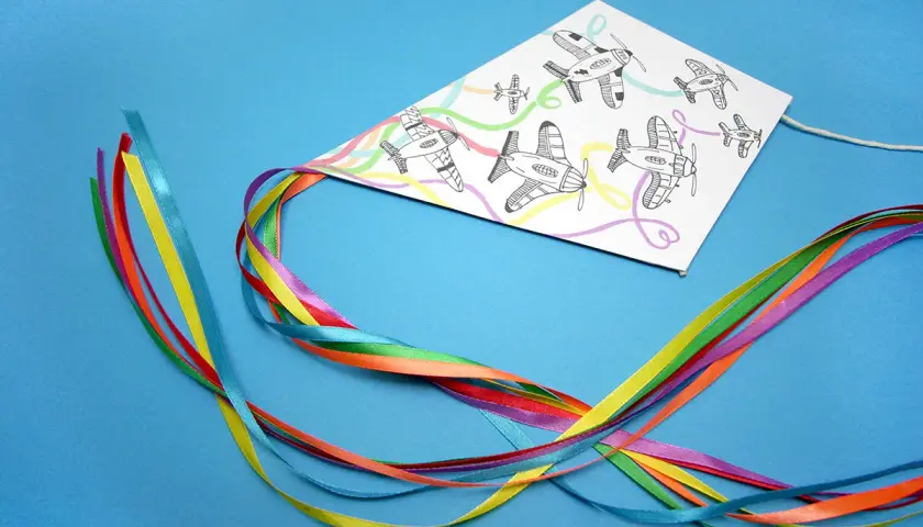 Kolorowy latawiec DIY z samolotami na tle niebieskim. Wstążki w tęczowych barwach tworzą ogon.