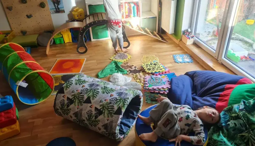 Dzieci bawią się na domowym torze przeszkód: tunel, ścieżka sensoryczna, ścianka wspinaczkowa i bujak.