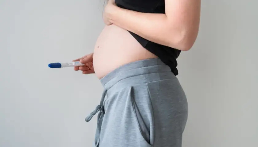 Kobieta w ciąży, trzymająca test ciążowy. Brzuszek widoczny, sugeruje 1 trymestr ciąży.