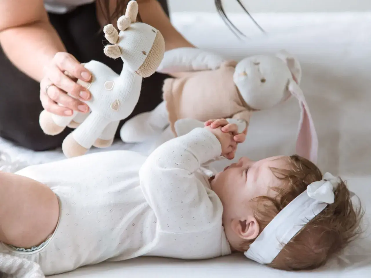 3 miesięczne dziecko nie chwyta zabawek, ale z zaciekawieniem patrzy na pluszową żyrafkę i królika podawane przez mamę.