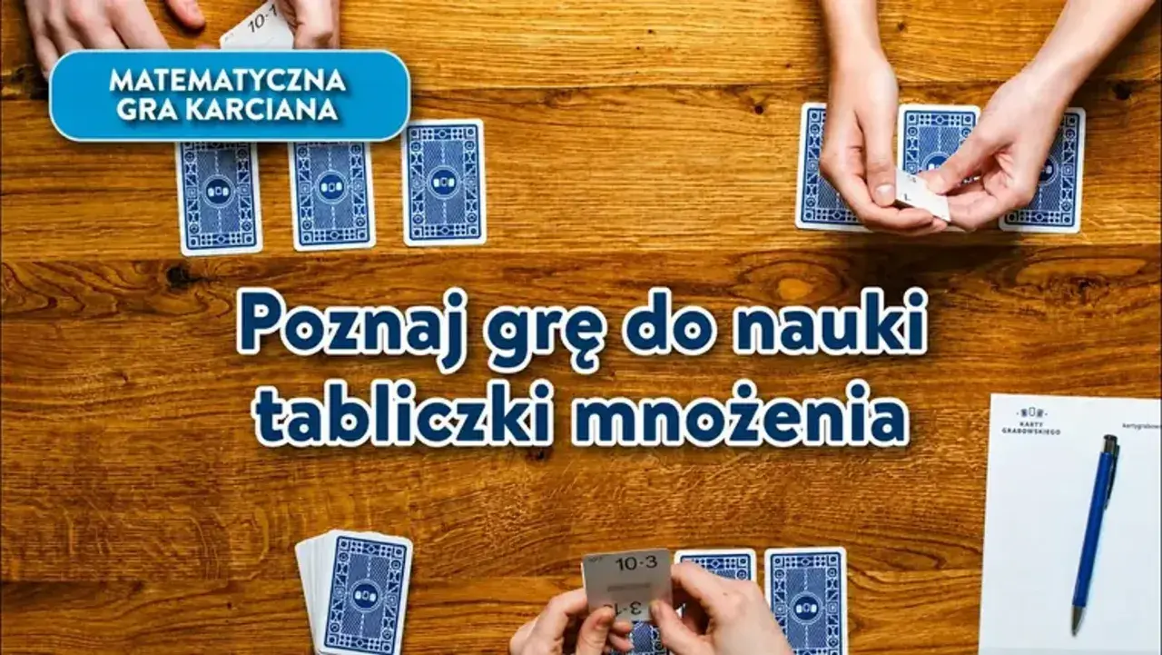 Gra karciana "Poznaj grę do nauki tabliczki mnożenia" na drewnianym stole. Dłonie trzymają karty z działaniami.