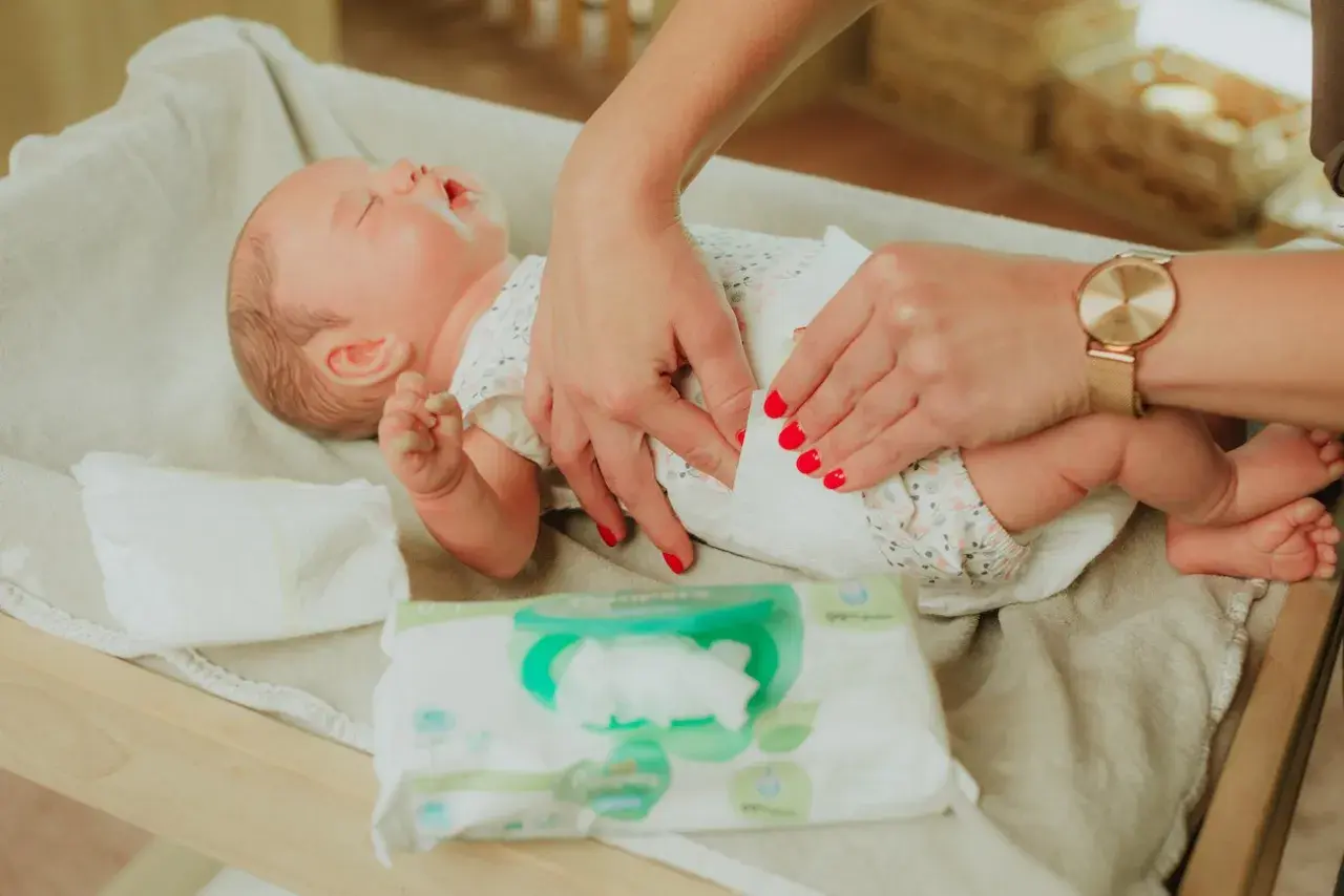 Delikatne dłonie mamy pokazują, jak przewijać noworodka, używając chusteczek nawilżanych.