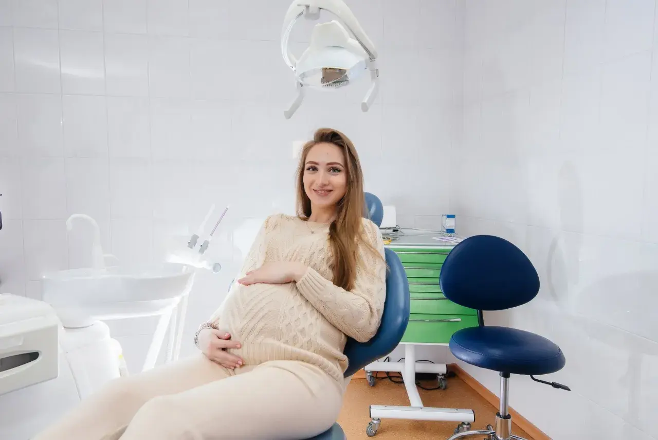 Uśmiechnięta, ciężarna dentystka w gabinecie, czeka na pacjenta.
