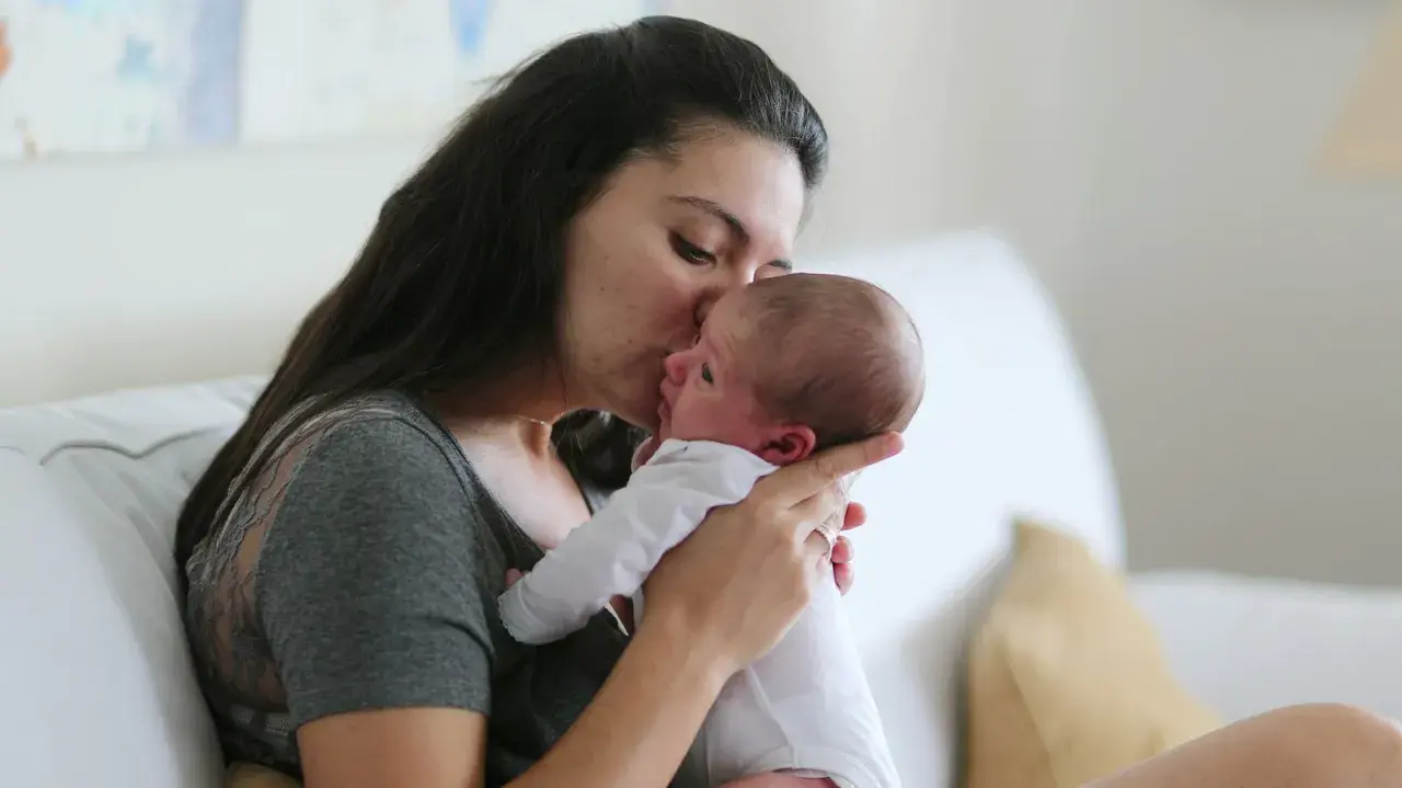 Ciepły uścisk mamy dla jej 6 tygodniowego dziecka. Delikatny pocałunek na czole maluszka.