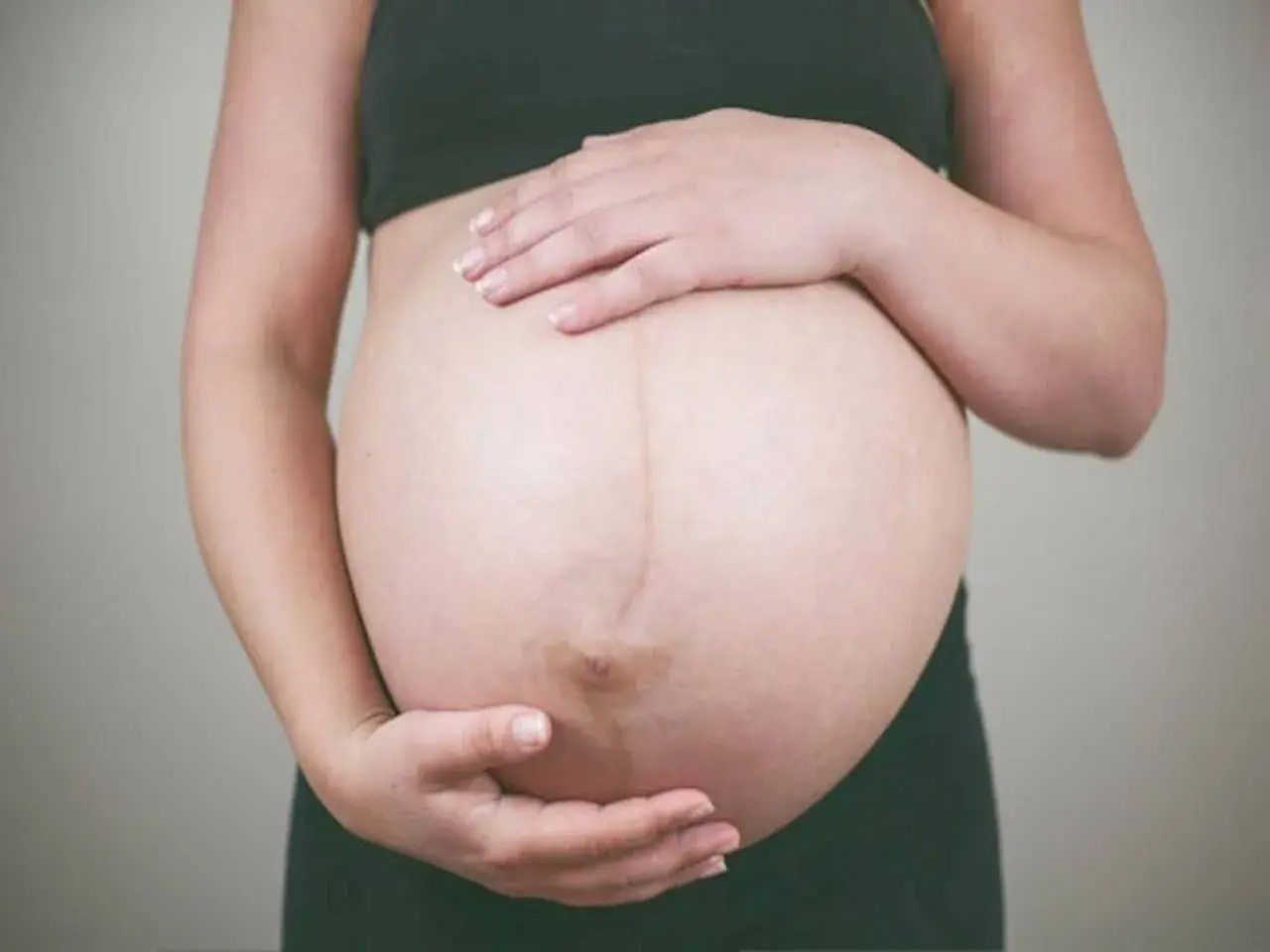 Dłońmi obejmuje zaokrąglony brzuch w ciąży. Widoczna ciemna linia biegnąca przez środek.
