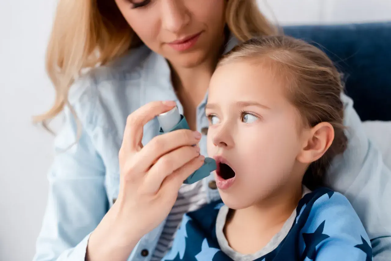 Mama pomaga córce z astmą wczesnodziecięcą użyć inhalatora.