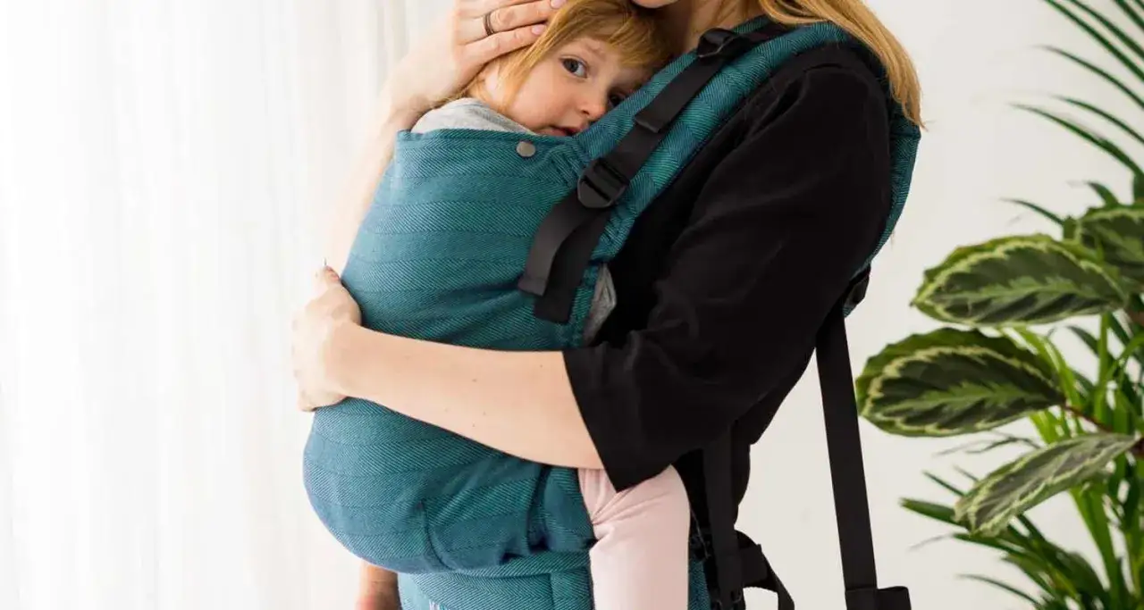 Mama tuli noworodka w turkusowym nosidle. Pokazuje, jak nosić noworodka blisko siebie.