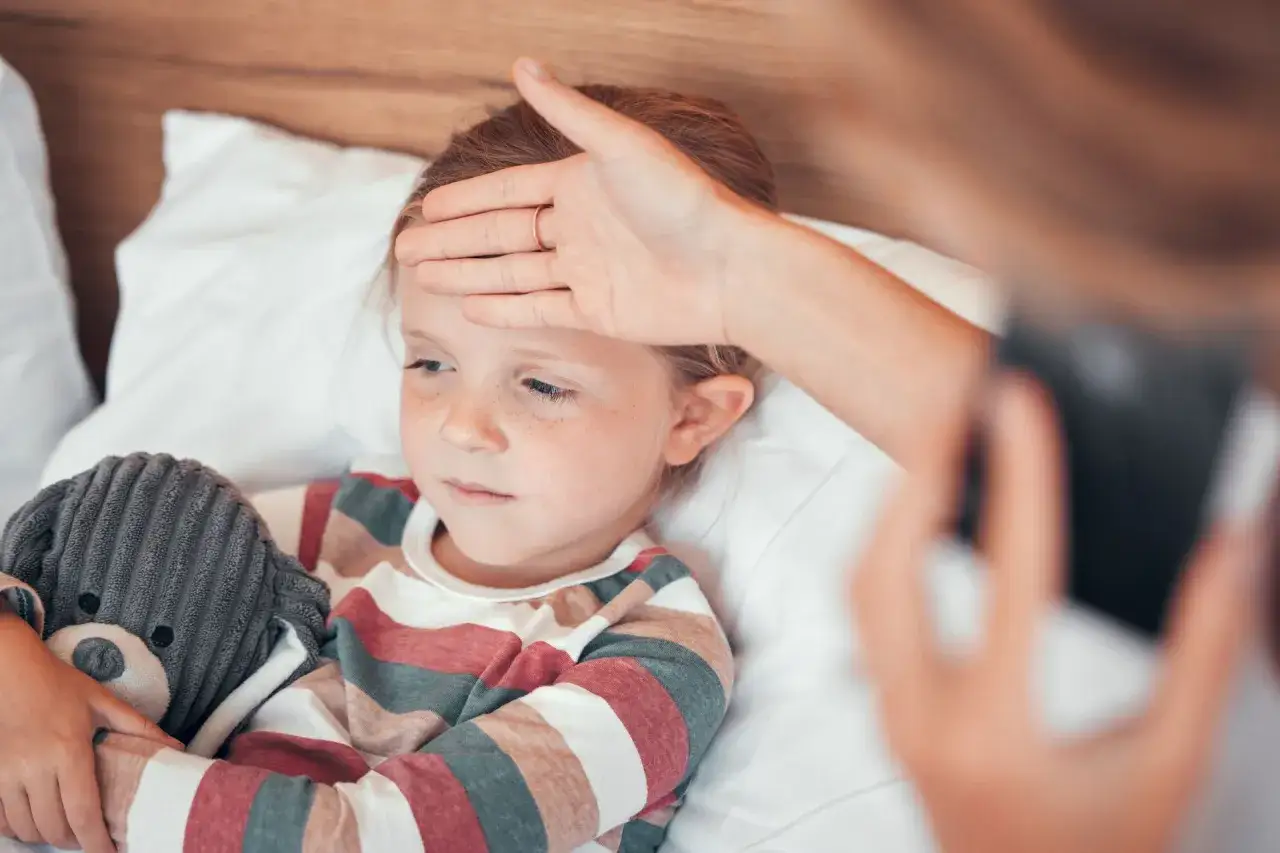 Dziecko z gorączką, mama sprawdza temperaturę. Wczesne meningokoki objawy mogą być mylone z grypą.