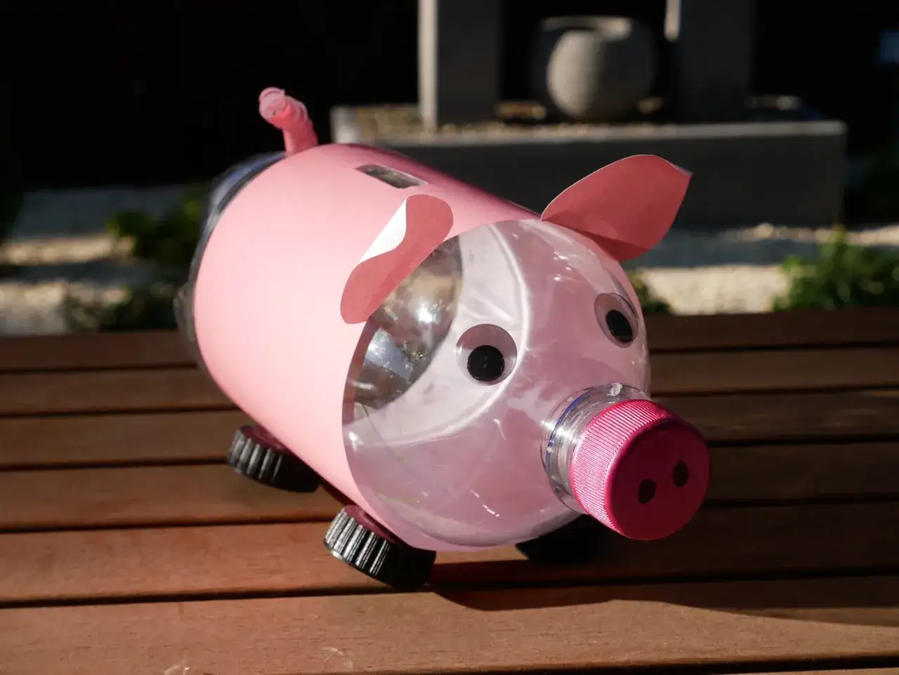 Urocza skarbonka diy z butelki, pomalowana na różowo, z kółkami i uszami z papieru. Idealna do nauki oszczędzania.