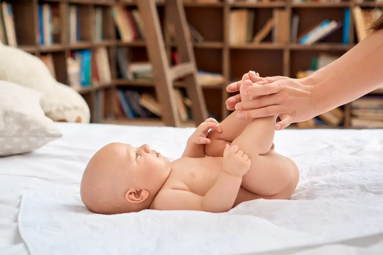 Niemowlę z bolesnymi gazami i brakiem kupy. Mama delikatnie masuje brzuszek maluszka, pr&oacute;bując przynieść mu ulgę.