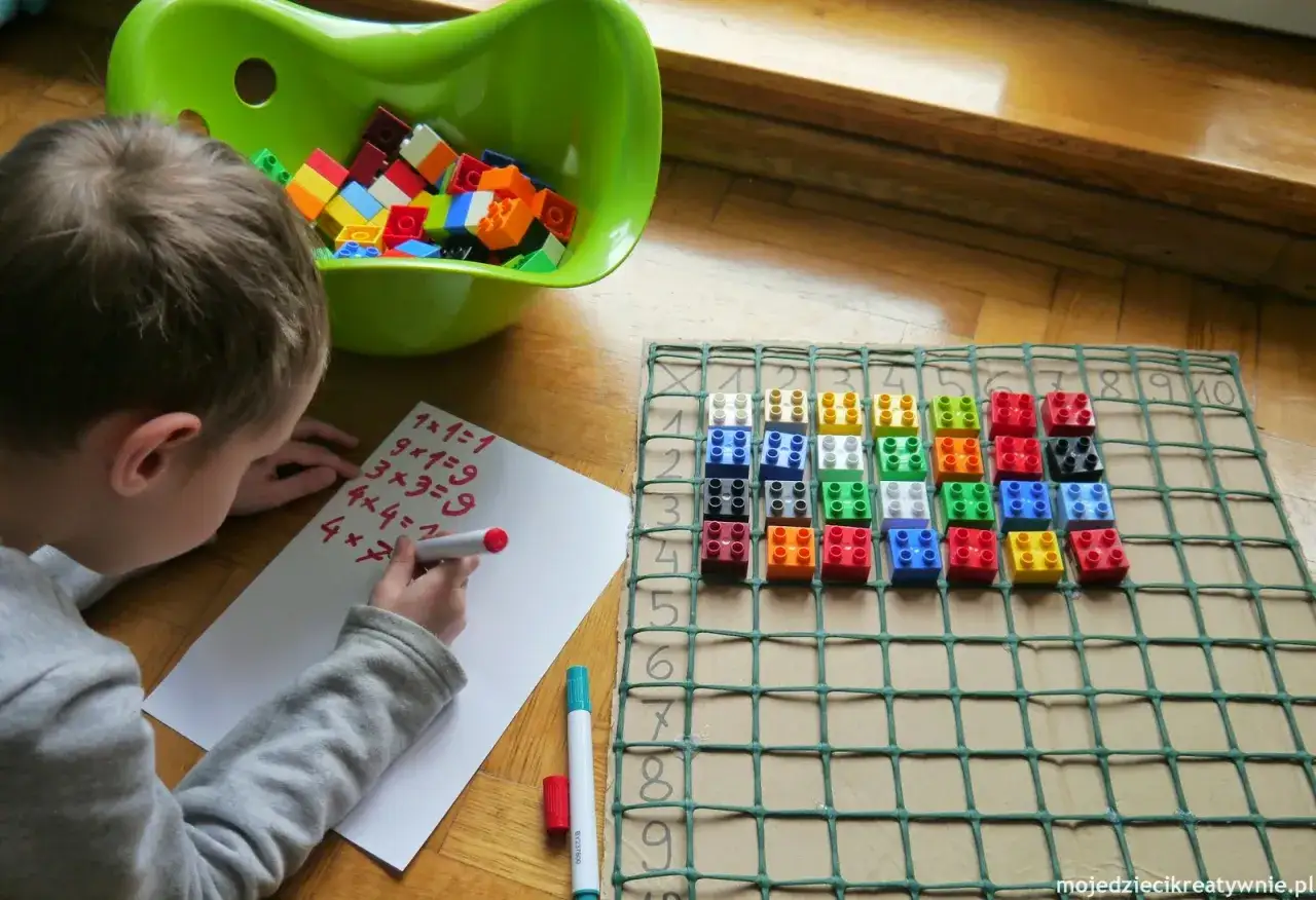 Chłopiec pisze zadania do nauki tabliczki mnożenia, używając klocków Lego do wizualizacji.